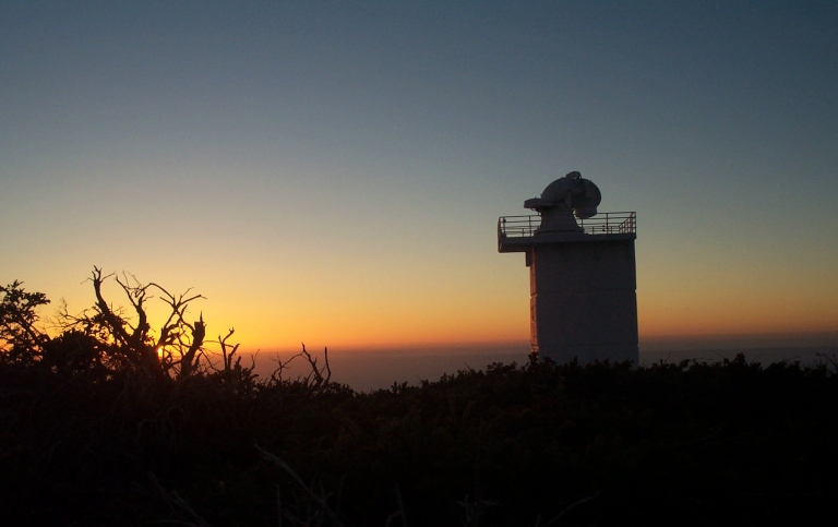 Colourful sunset in the background. Telescope in forefront.